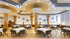 A large, well-lit hotel restaurant with multiple dining tables and a decorative ceiling - Pride Premier Dehradun