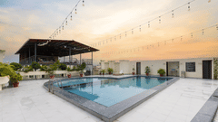 An inviting rooftop swimming pool is set against a colourful sunset sky with string lights overhead - Pride Premier Dehradun