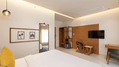 A modern hotel bedroom with a large white bed, a bedside table, a mounted television, and contemporary decor - Pride Premier Dehradun
