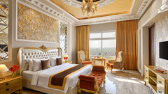 a double bed, a bench beside the bed, armchairs beside a coffee table, a television in the PREMIER ROOM - Royal Kingdom Sarovar Portico, Pilibhit