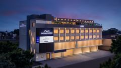 An exterior view of a hotel building with dark grey and beige facade and lit windows at Sarovar Portico, Hanumangarh.
