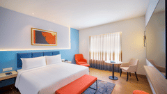 A clean and modern hotel room with a large bed, a desk and chair, and a pop of orange color in the decor | Executive Room | Sarovar Portico, Sriperumbudur