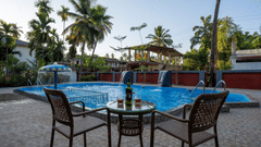 Chairs and a small table kept in front of a swimming pool with trees in the background - VITS Select Casuarina Diveagar