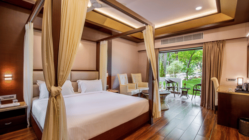 A spacious and elegant bedroom with a king-size bed, wooden flooring, and large windows offering views of lush greenery outside - Black Thunder, Coimbatore