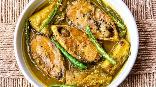 Bengali fish curry in mustard sauce garnished with green chillies, a classic Bengali seafood dish.