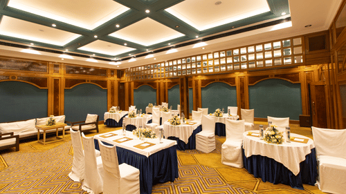 Luxurious banquet space with intricate carpet design, wood-paneled walls, round tables with formal settings, and ambient ceiling lighting.