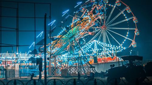 A ferris wheel lit up at night with other fairground attractions visible in the background.