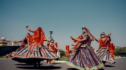 Several people in patterned skirts and head coverings perform a dance on a paved surface.