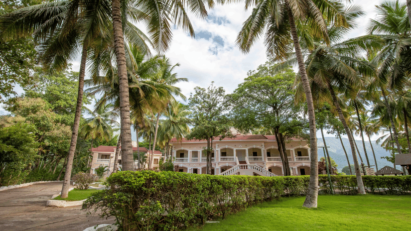 Expansive green lawn with coconut trees, leading to a shaded seating area with a view of resort buildings in the background - Black Thunder, Coimbatore