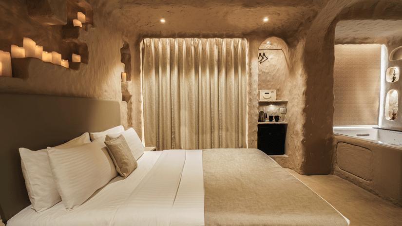 Cave Room at Dragonfly Hotel- The Art Hotel with textured stone?like walls and ceiling, large bed with beige bedding, curtain over alcove, built?in shelves with soft lighting, and recessed ceiling lights.