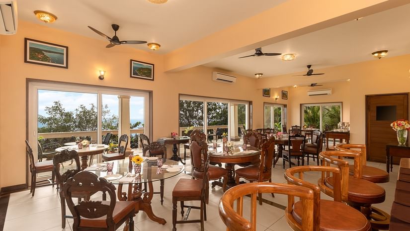 A dining area with fans, ceiling lights, high chairs, a bar counter and stunning views - Highland Sarovar Portico, Sindhudurg