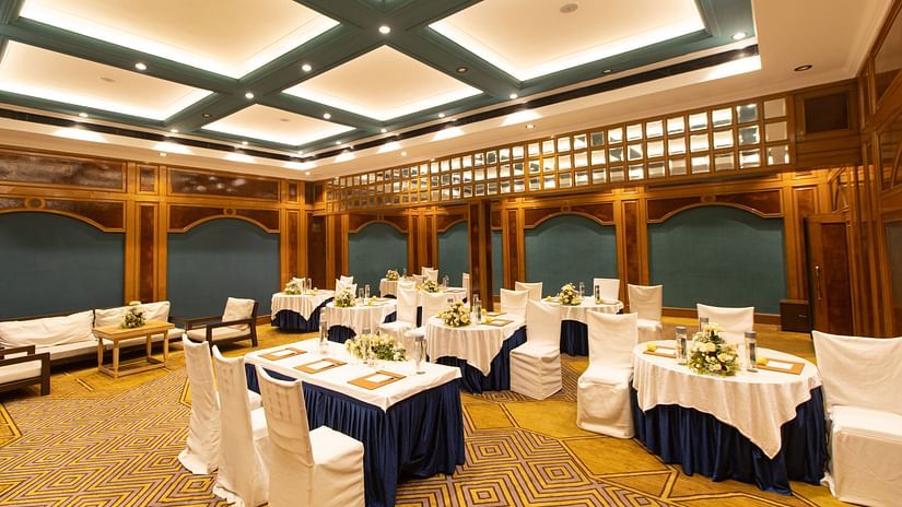 Luxurious banquet space with intricate carpet design, wood-paneled walls, round tables with formal settings, and ambient ceiling lighting.