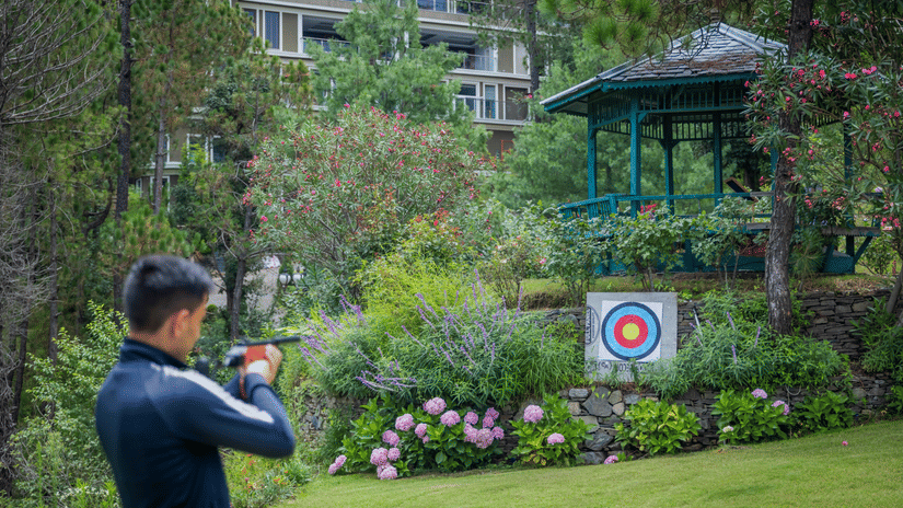 Guest practicing archery in the lush gardens of The Manor Sports & Wellness Hotel, a wellness resort in Shimla.