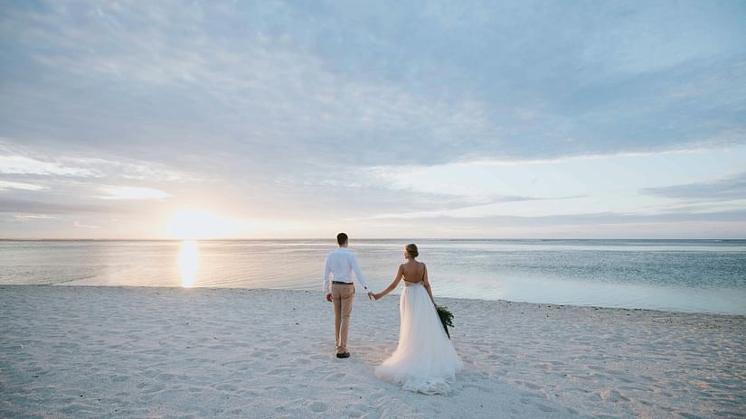 A couple walking hand in hand towards the sunset on the beach with white sands