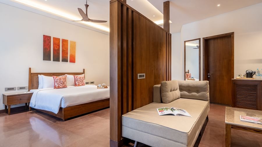 An image of a bedroom with partition, on one side there is a bed and on the other there is a seating area with sofa and table