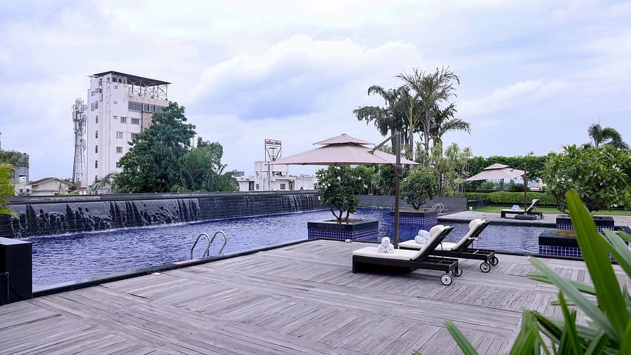 A serene poolside area with lounge chairs, umbrellas, and a calming water feature with lush greenery in the background - Balaji Sarovar Premiere, Solapur