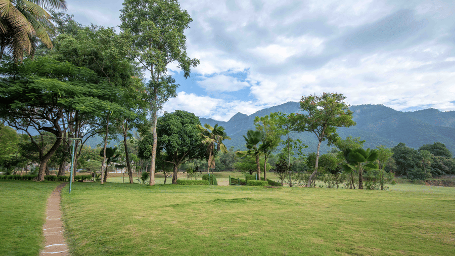 Large open lawn with a pathway leading into the distance, surrounded by trees and mountains in the background - Black Thunder, Coimbatore