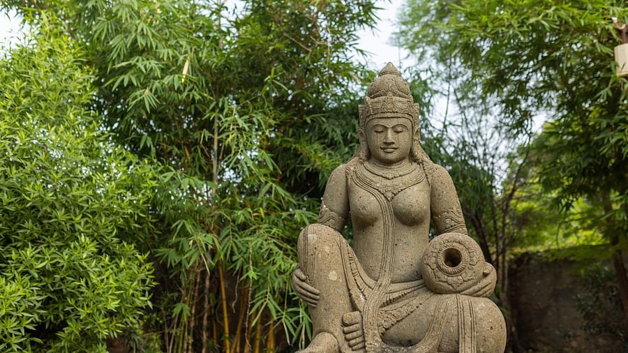 Statue of a lady holding an earthen pot with a backdrop of lush trees at Clarks Safari, Ranthambore.