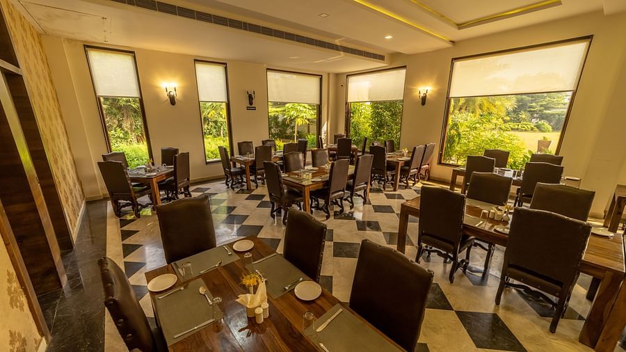 A well-lit dining area at Clarks Safari, Ranthambore, with multiple tables and chairs, offering views of the surrounding landscape.
