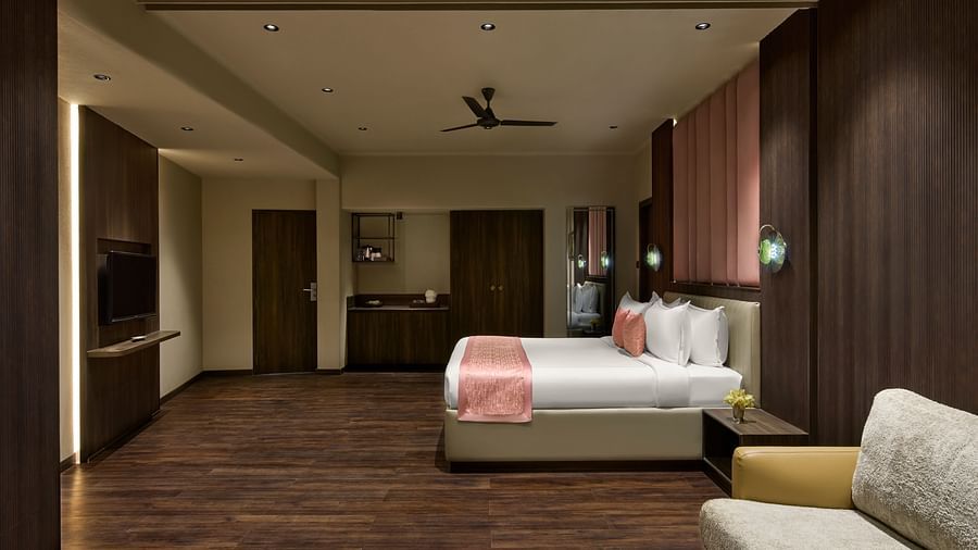 Junior Suite with a large bed, a sofa, and a television, featuring warm lighting and wooden accents at DGV Resort by Treat, Silvassa.