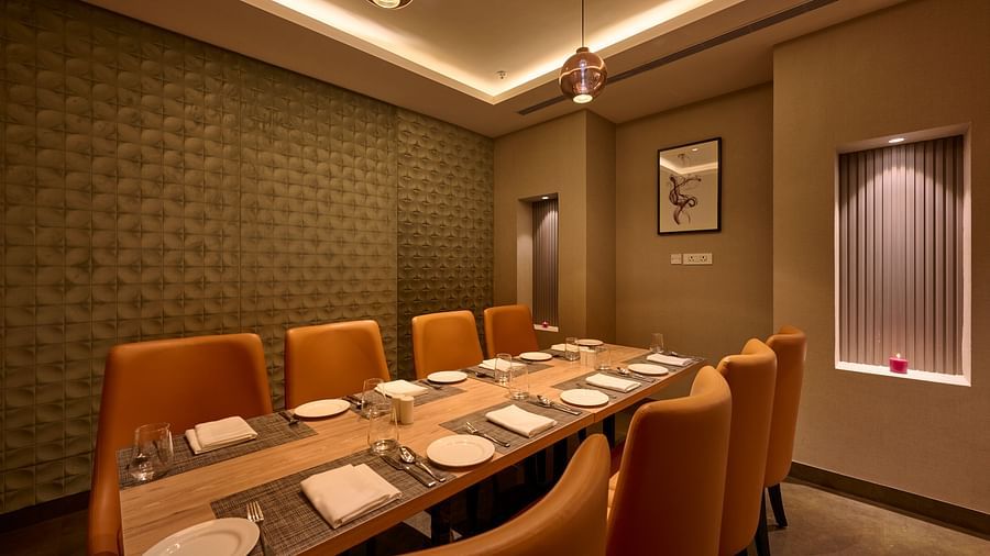 A secluded dining area with a long table, comfy orange chairs and ambient lighting