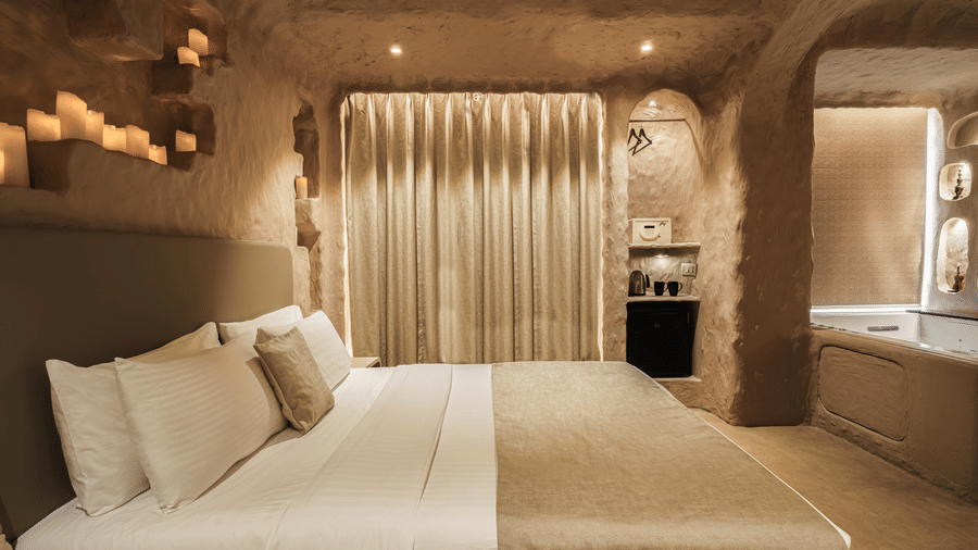 Cave Room at Dragonfly Hotel- The Art Hotel with textured stone?like walls and ceiling, large bed with beige bedding, curtain over alcove, built?in shelves with soft lighting, and recessed ceiling lights.