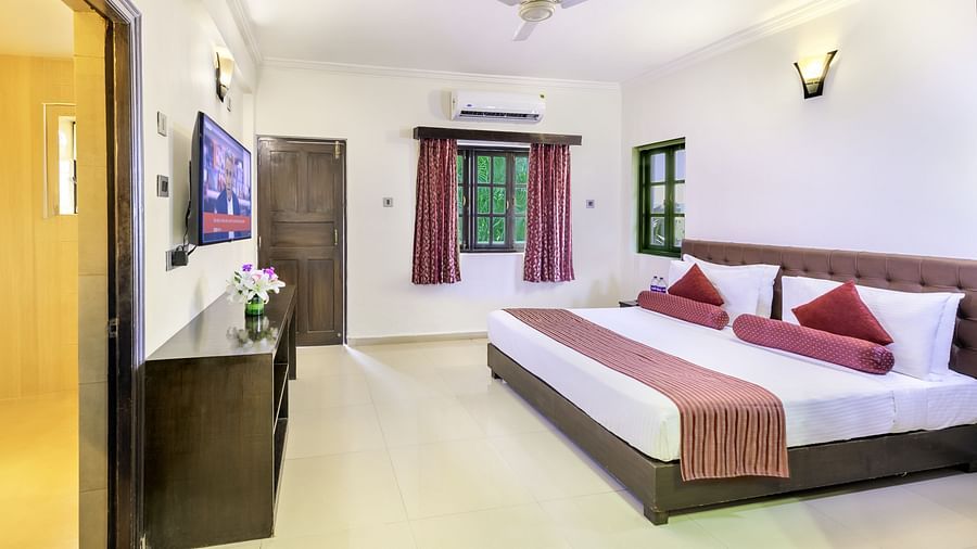 a bedroom featuring a double bed, a ceiling fan, a wall-mounted television, and a window with verdant views - Golden Tulip, Candolim, Goa