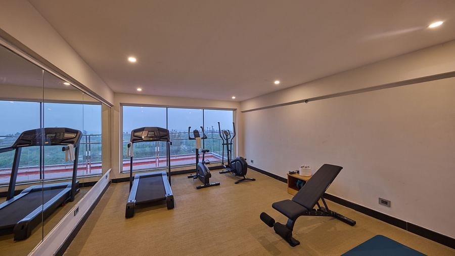 a treadmill, a stationary bike, an elliptical trainer, and a bench in the fitness centre at Grand Continent, Mahabalipuram