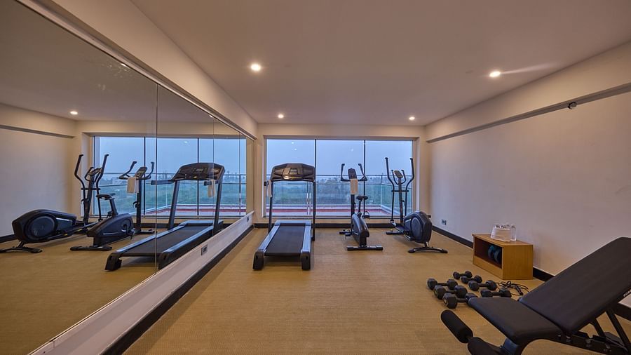 a treadmill, a stationary bike, an elliptical trainer, and a bench in our fitness centre at Grand Continent, Mahabalipuram