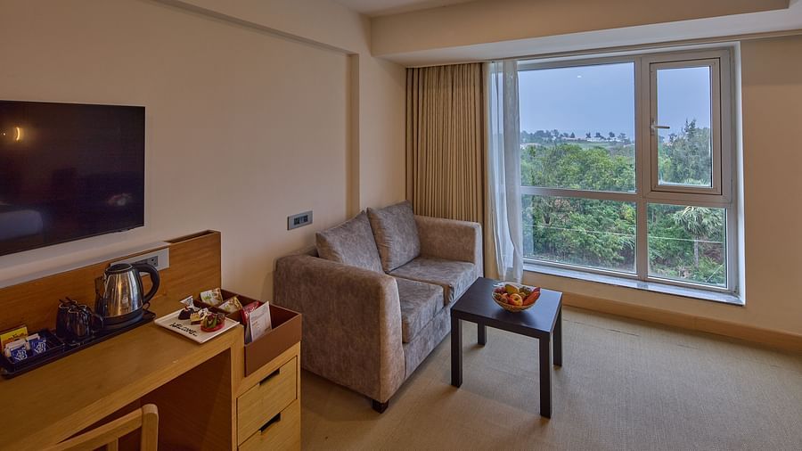 a television above a large table with a minibar section and a sofa beside a large window in The Grand Suite Sea View at Grand Continent, Mahabalipuram
