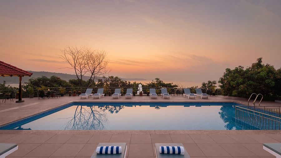 An outdoor pool seen during a sunset with sun loungers on its deck - Highland Sarovar Portico, Sindhudurg