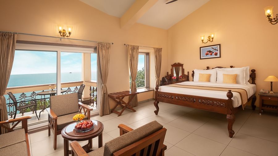 A room featuring a bed with wooden frame, a seating area and a balcony with stunning vistas - Highland Sarovar Portico, Sindhudurg