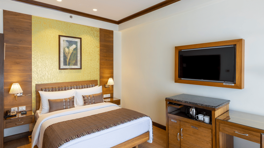 Business Club Room with a bed, wooden TV console and framed artwork at Kenilworth Hotel, Kolkata.