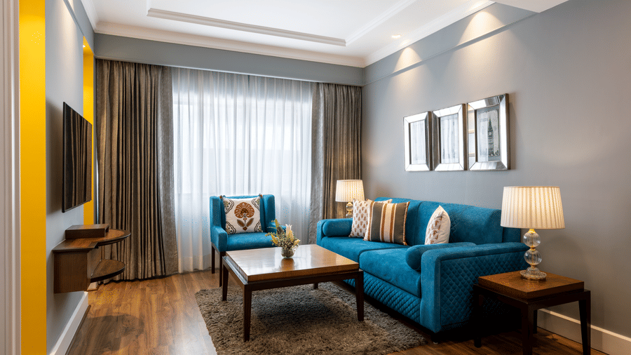 Junior Suite lounge area with a blue sofa, coffee table and framed art at Kenilworth Hotel, Kolkata.