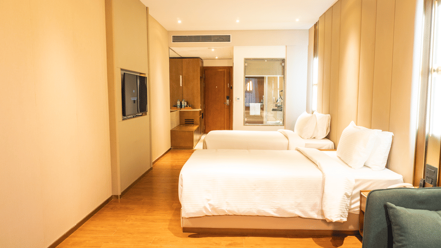 Single beds side by side, a wooden wardrobe cabinet near the entryway, and a glass partition wall at Pride Plaza Indore.