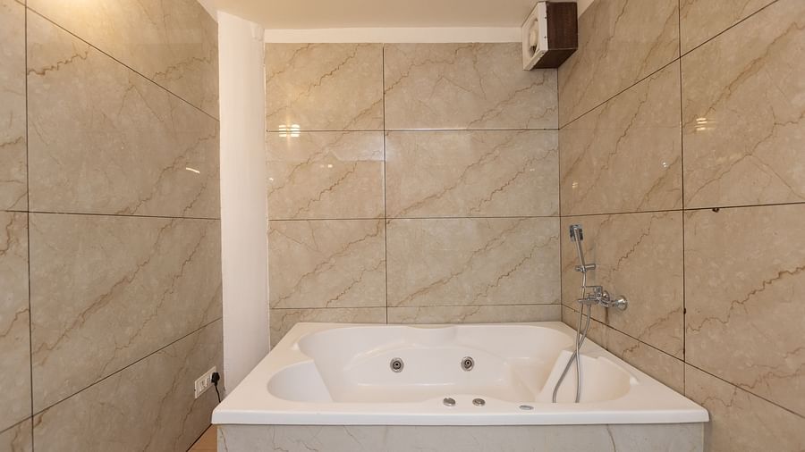 A modern bathroom with light-coloured tiled walls, featuring a white built-in Jacuzzi bathtub - Pride Premier Dehradun