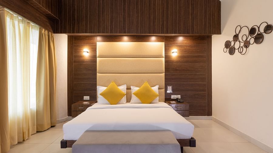 A neatly presented hotel bedroom with a large bed, a light-coloured padded headboard, and dark wood accents on the wall behind it - Pride Premier Dehradun