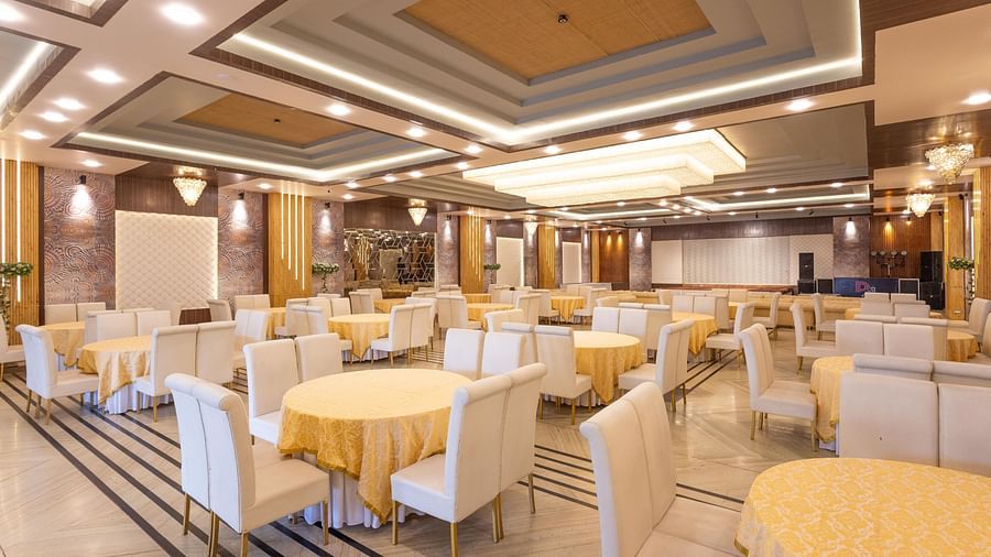 A spacious banquet hall is decorated with elegant cream and gold tables and chairs, ready for an event - Pride Premier Dehradun