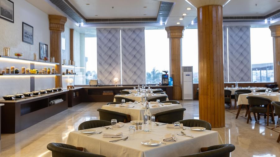 A refined hotel dining room set up for a formal meal, with a buffet table visible on the left - Pride Premier Dehradun