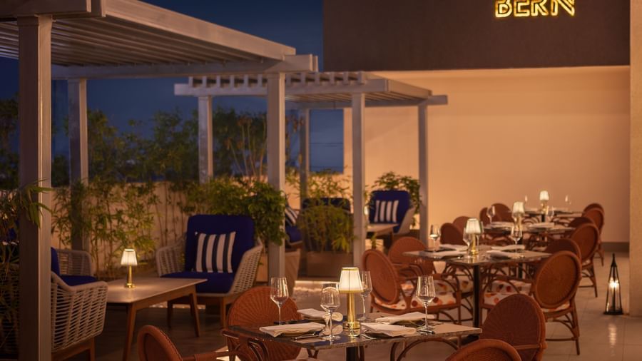 A hotel rooftop restaurant with a beige facade, brown wicker chairs, and tables at Sarovar Portico, Hanumangarh.