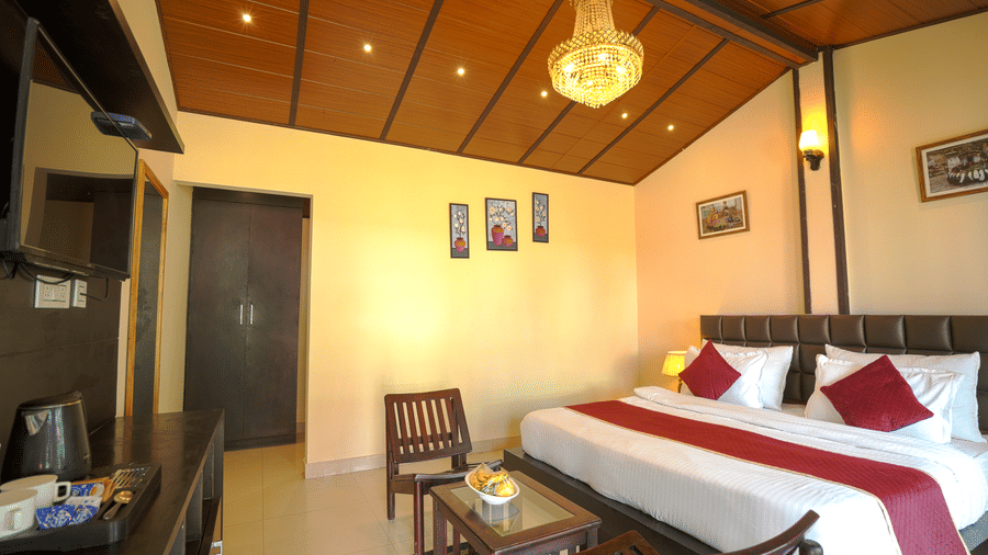 A room with a wooden roofing and a chandelier adding charm, to a king bed with cushions, 2 chairs and a coffee table, with decors like wall hanged paintings 