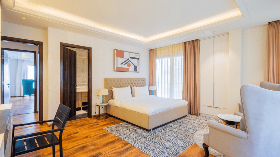 A spacious and best place to stay in Shimla, featuring Premium Apartment bedroom at The Manor Luxury Apartments with a double bed, patterned rug, an armchair, and wooden flooring.