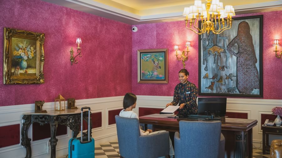 Stylish reading lounge or office with red accent walls, antique paintings, and blue modern chairs.