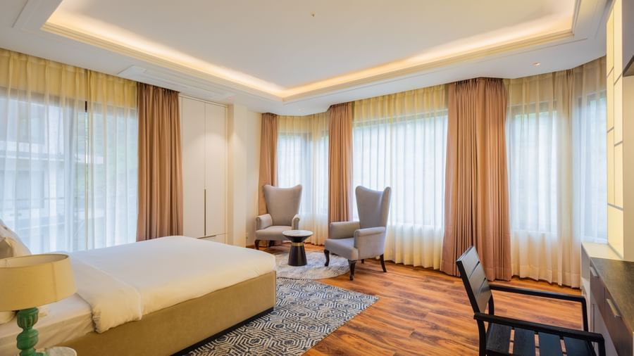 Spacious guest suite with large windows, warm wooden flooring, and a clean, modern design, displaying the elegant accommodation options at The Manor Sports & Wellness Hotel in Shimla.