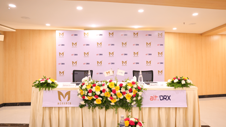 A conference stage arrangement in Coronet Ball Room at The Monarch Hotel, Brigade Road with a long table backdrop branding and floral decor.
