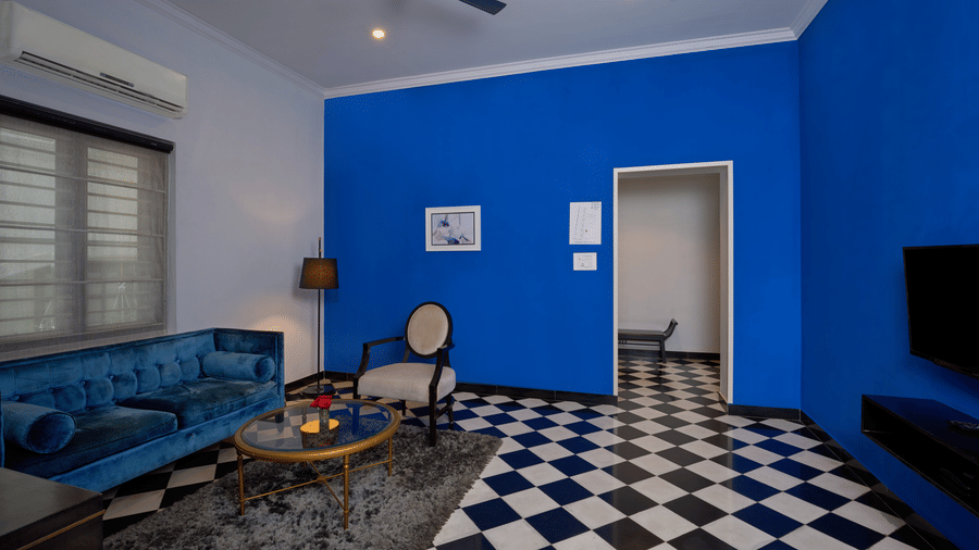 Modern living room inside The Old Court House by Abad, one of the luxury suites in Kochi, featuring a vibrant blue accent wall, checkered black and white flooring, a plush blue velvet sofa, and contemporary decor.