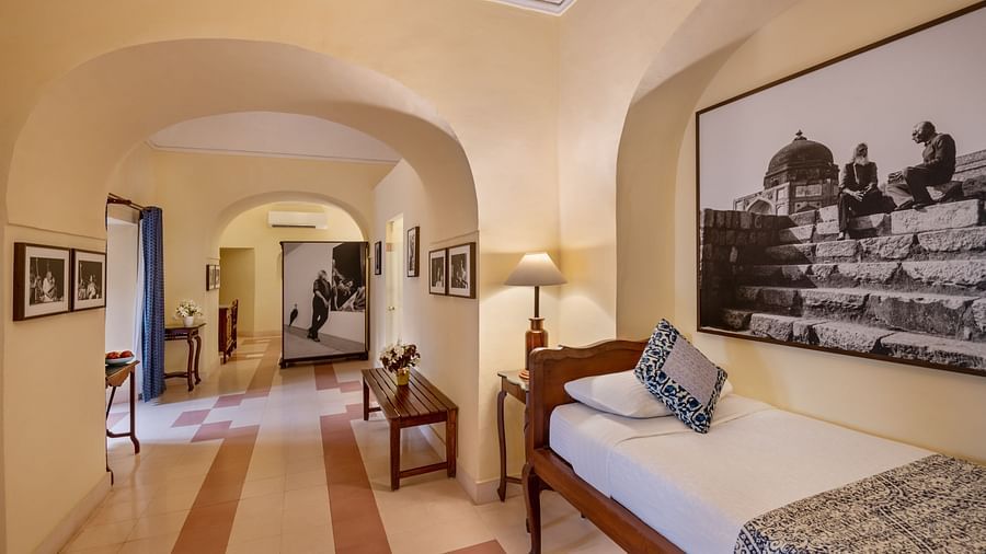 Room with single bed, patterned pillow and runner, furniture including tables, lamp, artwork, arched doorways, and patterned floor - Tijara Fort-Palace - 19th Century, Alwar.