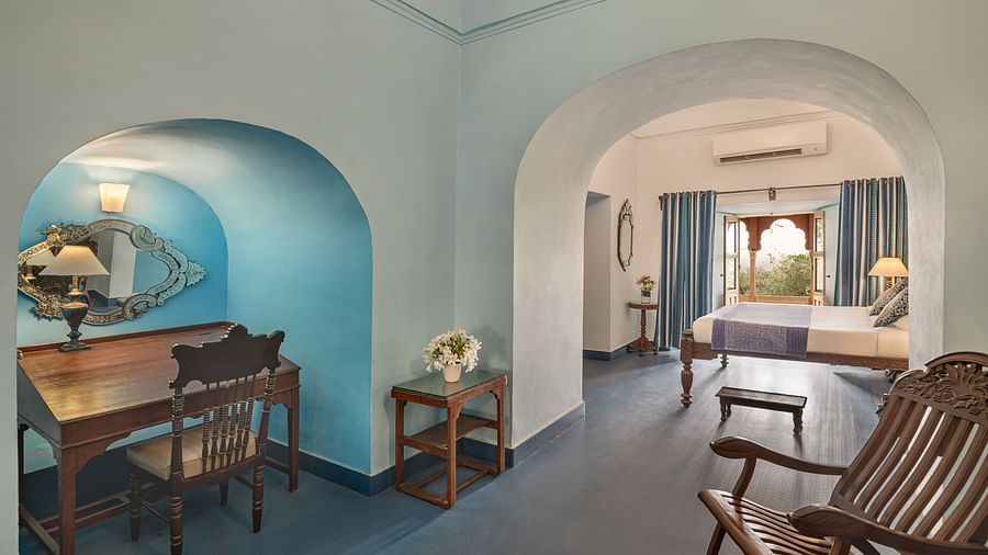 Room with desk, chair, table, mirror in arched alcove, rocking chair, and view into another room with bed, curtains, and arched doorway - Tijara Fort-Palace - 19th Century, Alwar.