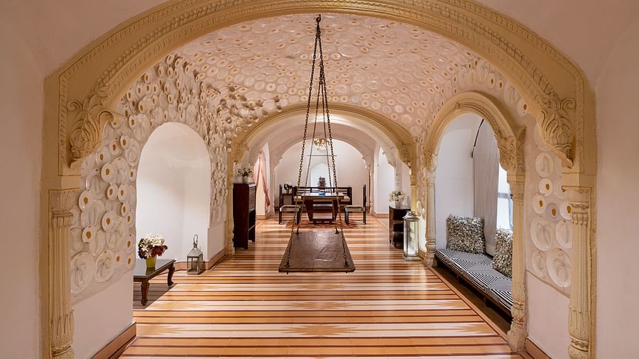 Hallway with arched doorways, patterned ceiling, furniture including tables and seating, decorative hanging element, and striped floor - Tijara Fort-Palace - 19th Century, Alwar.