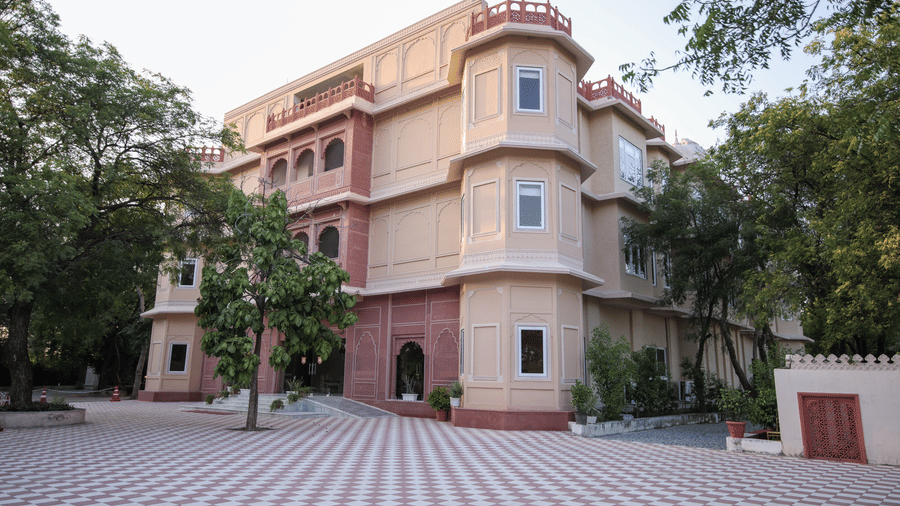 A view of the facade of Ranbanka Ballroom with a large courtyard, trees, and blue sky in the background.